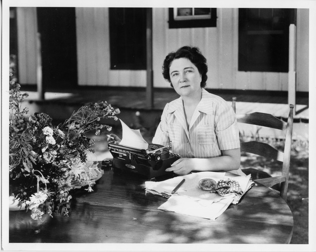 Marjorie Kinnan Rawlings In Her Yard, Seated At Table With Typewriter And Flowers