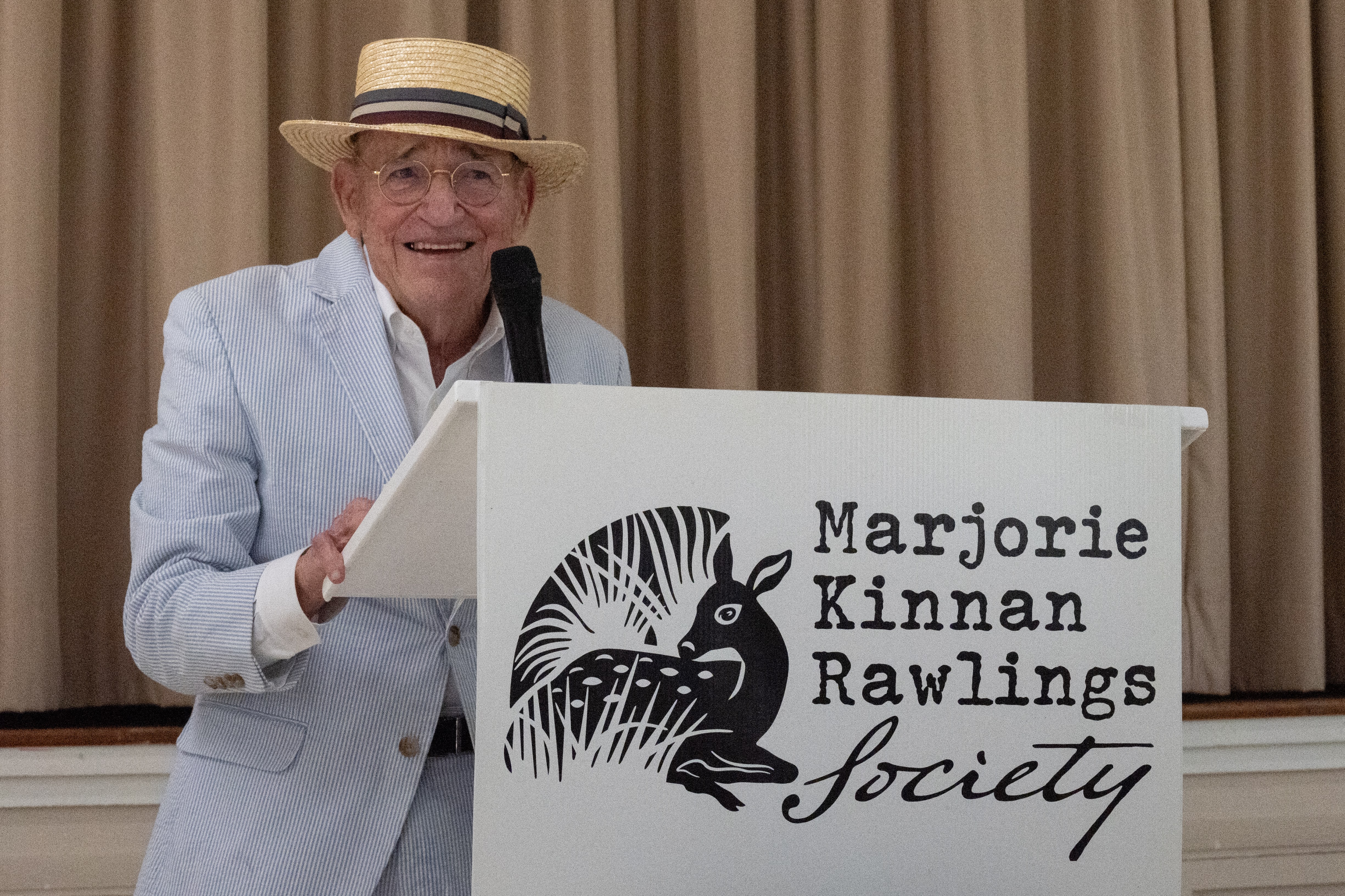 Buddy Jacobs standing behind a podium with a sign saying the Marjorie Kinnan Rawlings Society